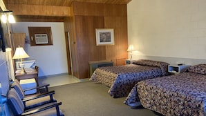 Habitación de hotel con dos camas, un escritorio con lámpara, una silla, techo de madera y un cuadro en la pared.