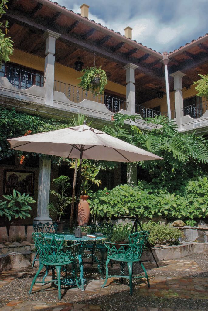 Eine Terrasse im Freien mit Tisch und Stühlen, umgeben von üppiger Bepflanzung und einem gefliesten Boden.
