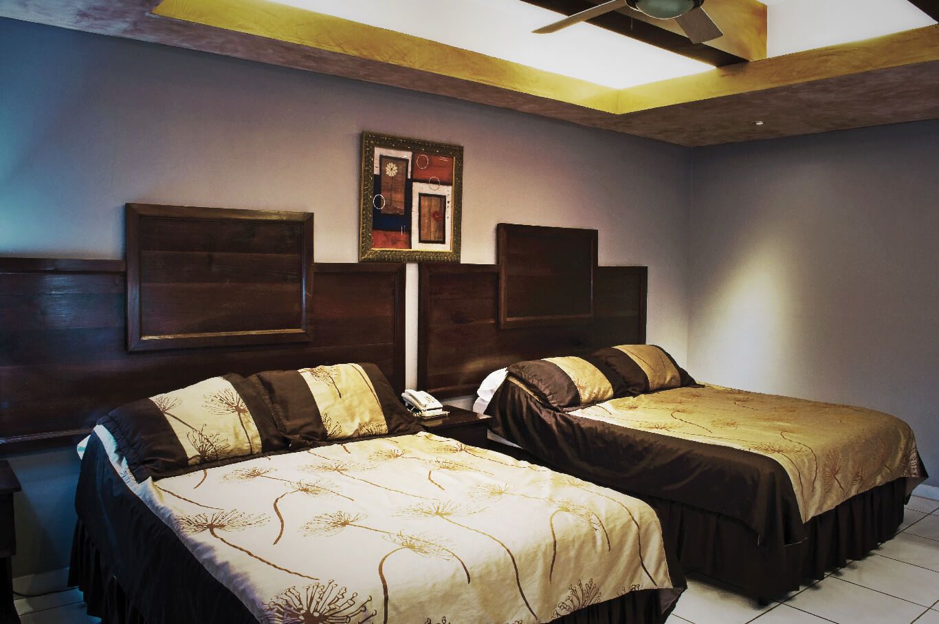 A hotel room with two beds, a ceiling fan, and artwork on the walls.