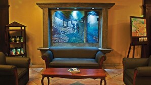 Un vestíbulo con un cuadro grande de un túnel, un sofá, dos sillones, una mesa de centro con un libro y una estantería con botellas.