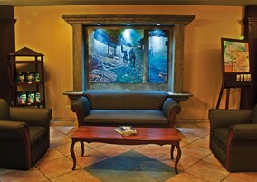 A lobby with a large painting of a tunnel, a sofa, two armchairs, a coffee table with a book, and a shelf with bottles.