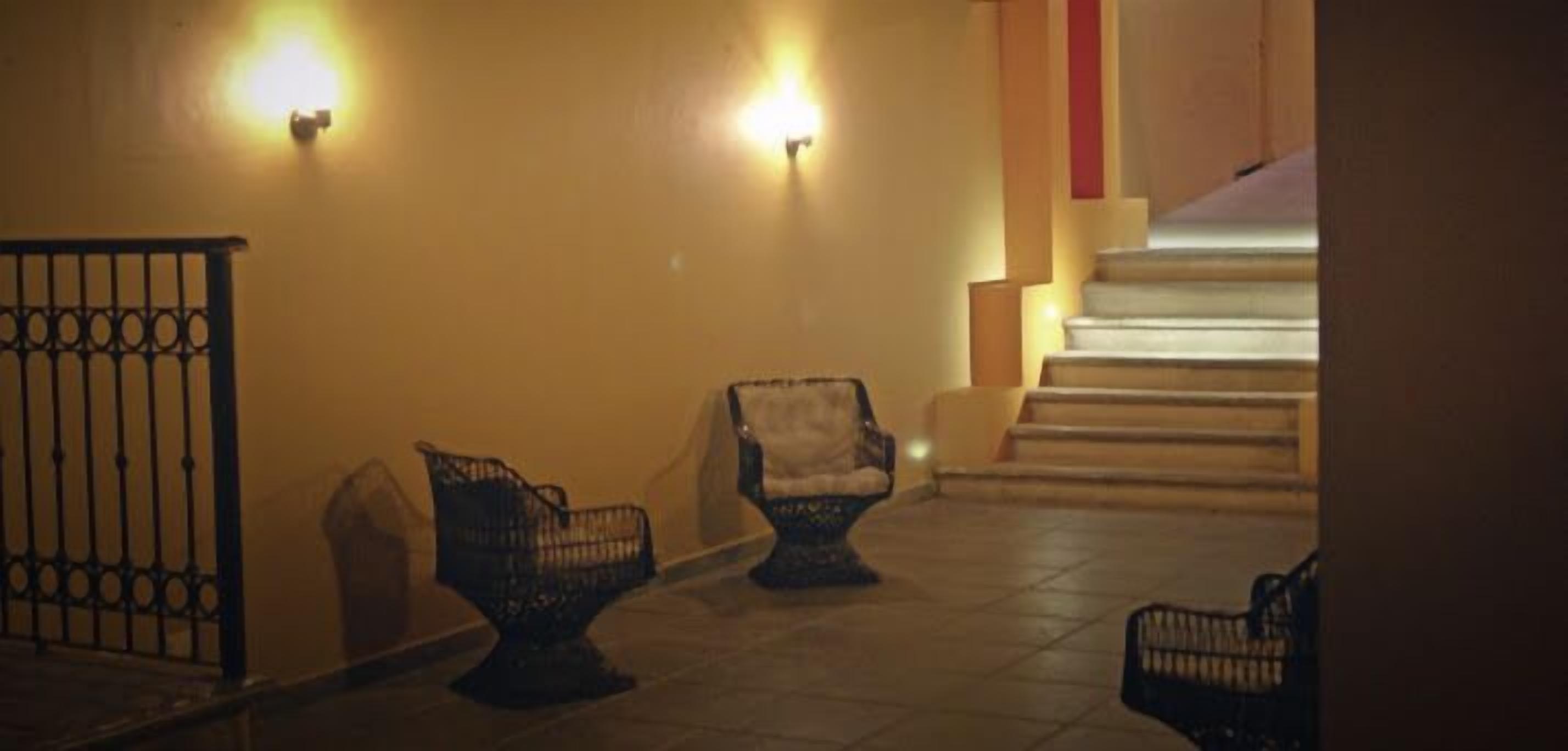 A dimly lit hallway with a staircase, two wicker chairs, and a metal railing.