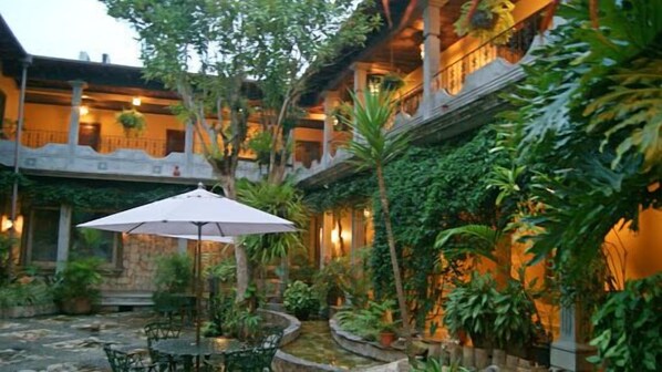 A courtyard with a central table and umbrella, surrounded by lush greenery and a stone wall.