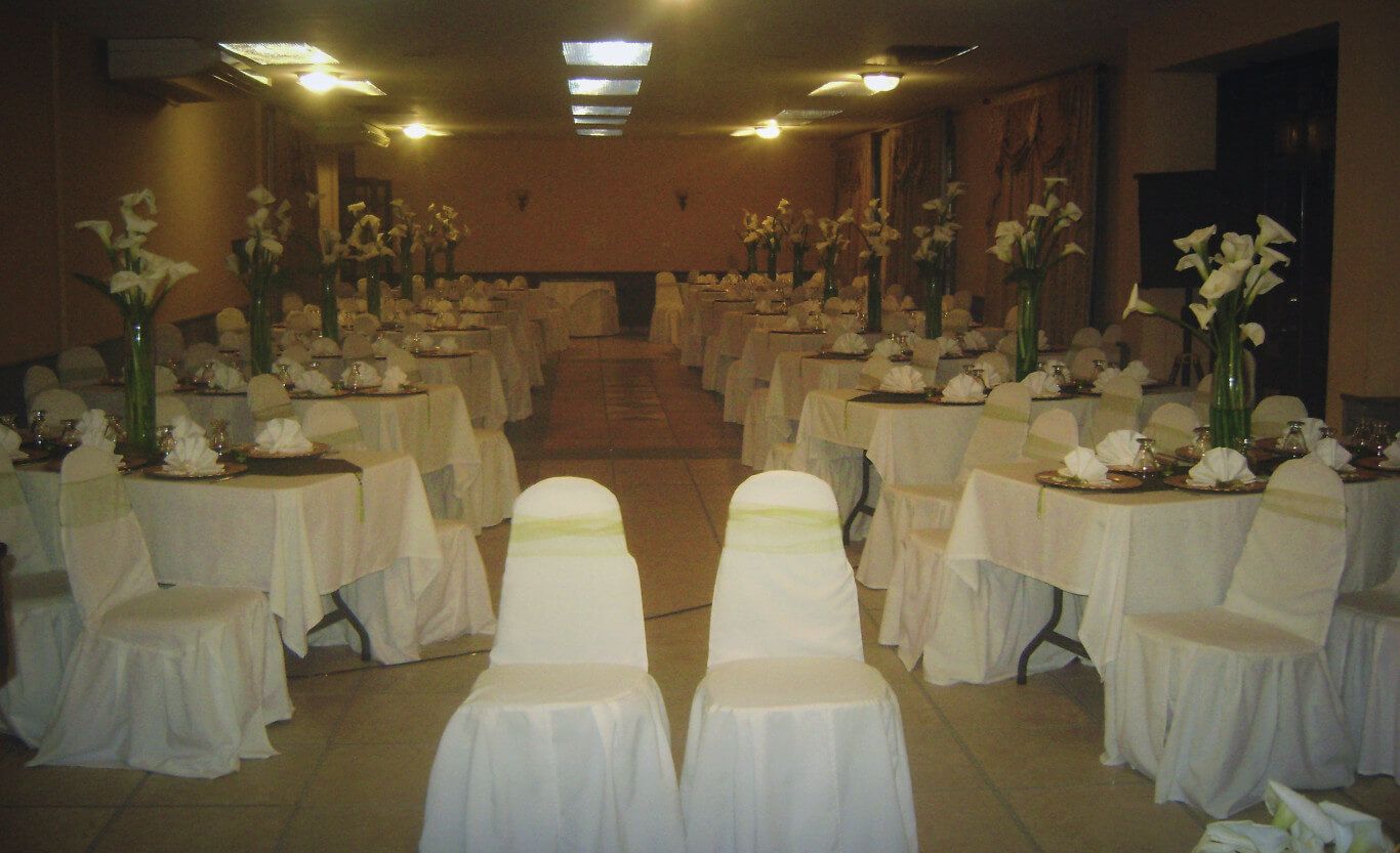 A banquet hall with rows of tables set for a formal event, each with white tablecloths and floral centerpieces.