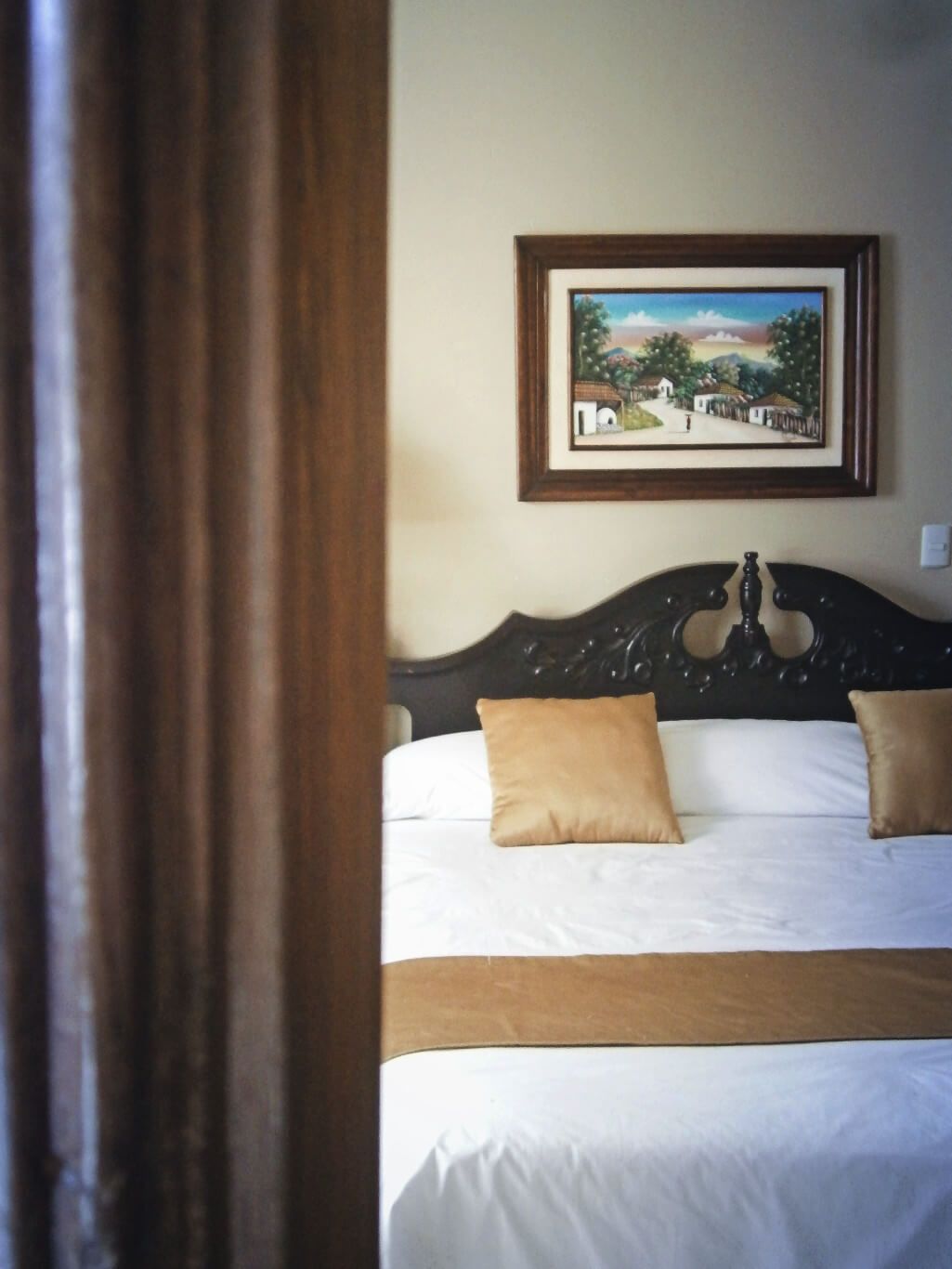 A bedroom with a bed, two pillows, a framed picture on the wall, and a wooden headboard.