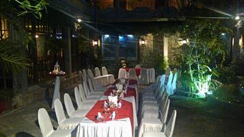 An outdoor dining area with tables set for a meal, surrounded by chairs and plants.