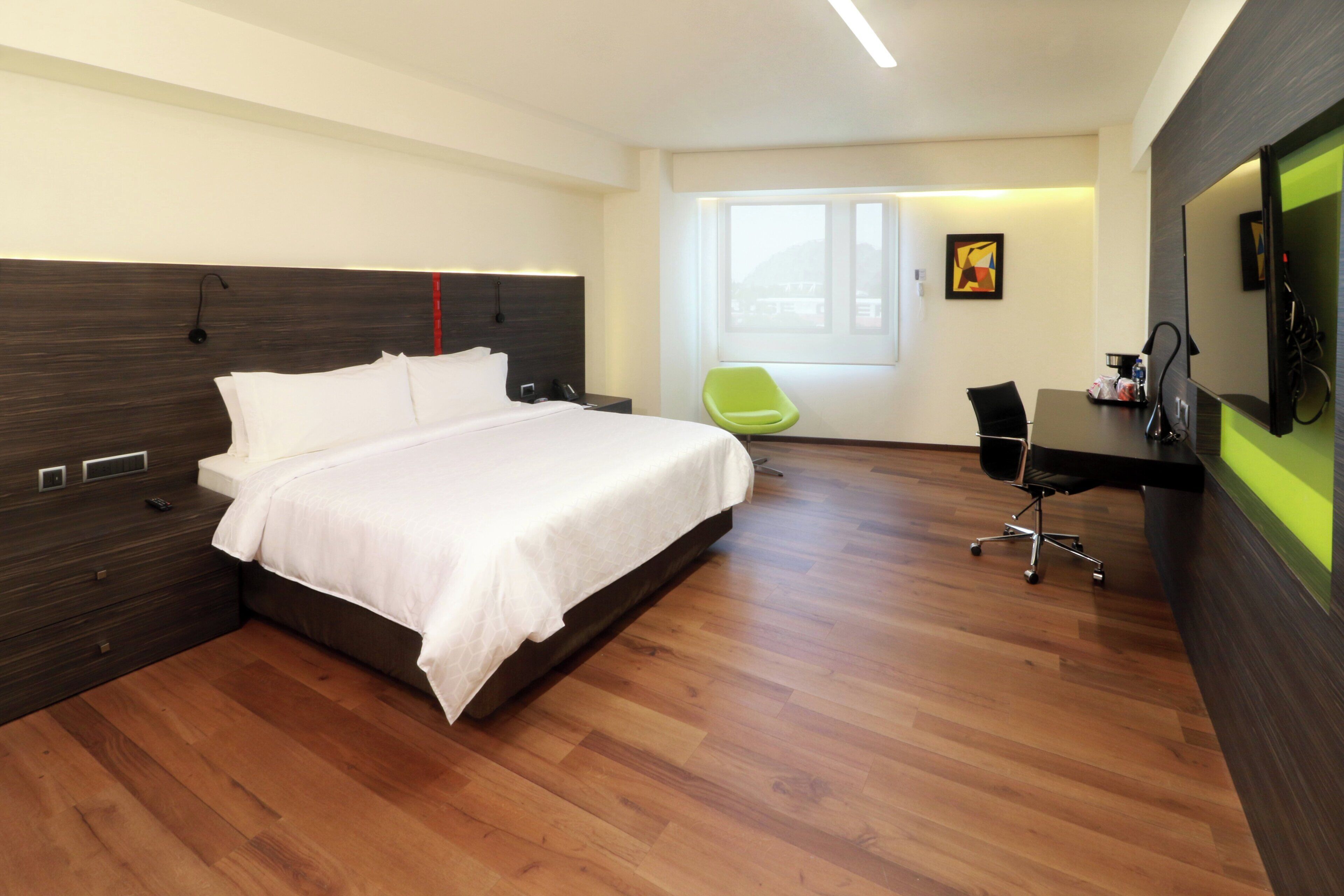 A modern hotel room with a large bed, a desk, a chair, and a television.