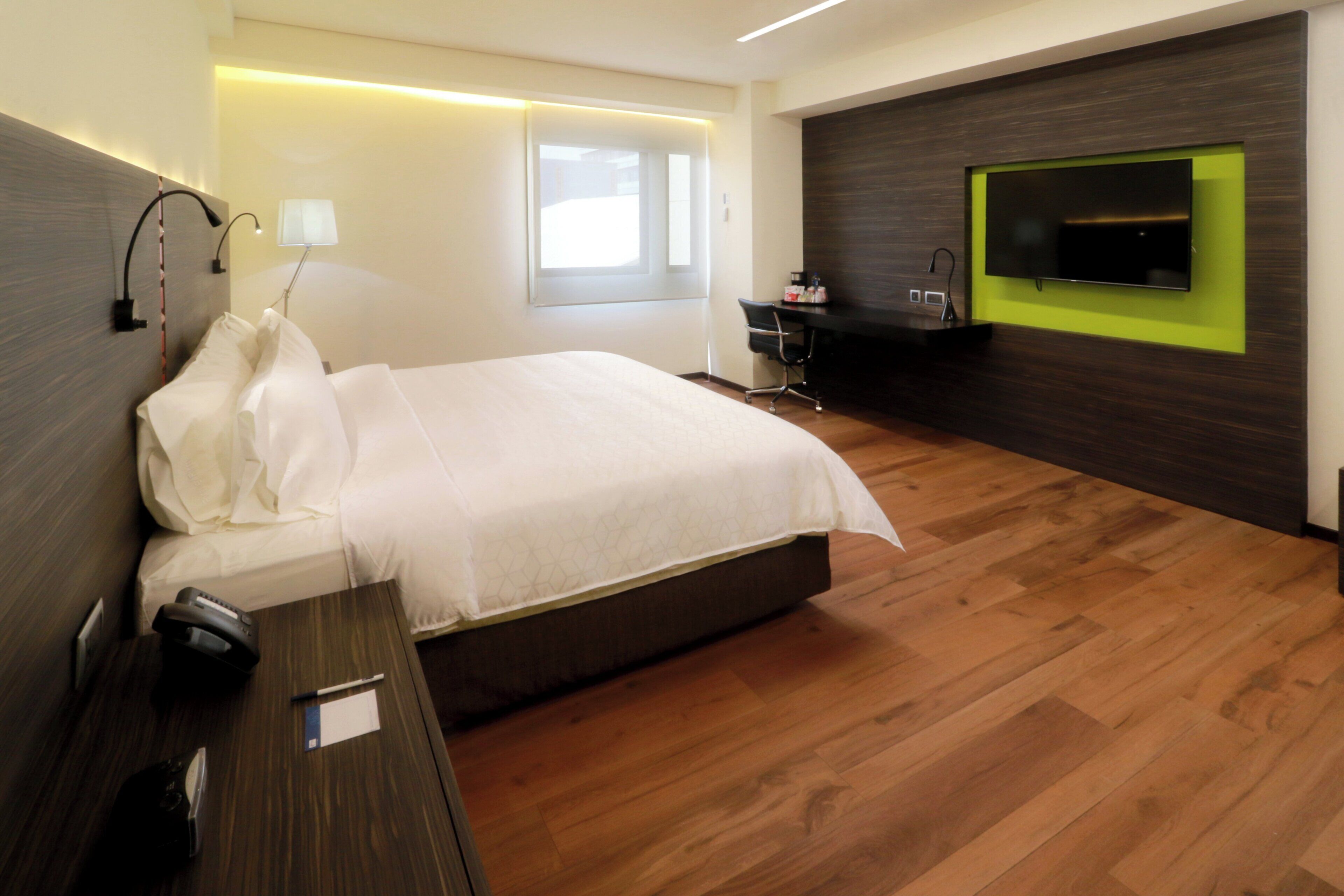 A modern hotel room with a large bed, a desk, a chair, a flat-screen TV, and a window.