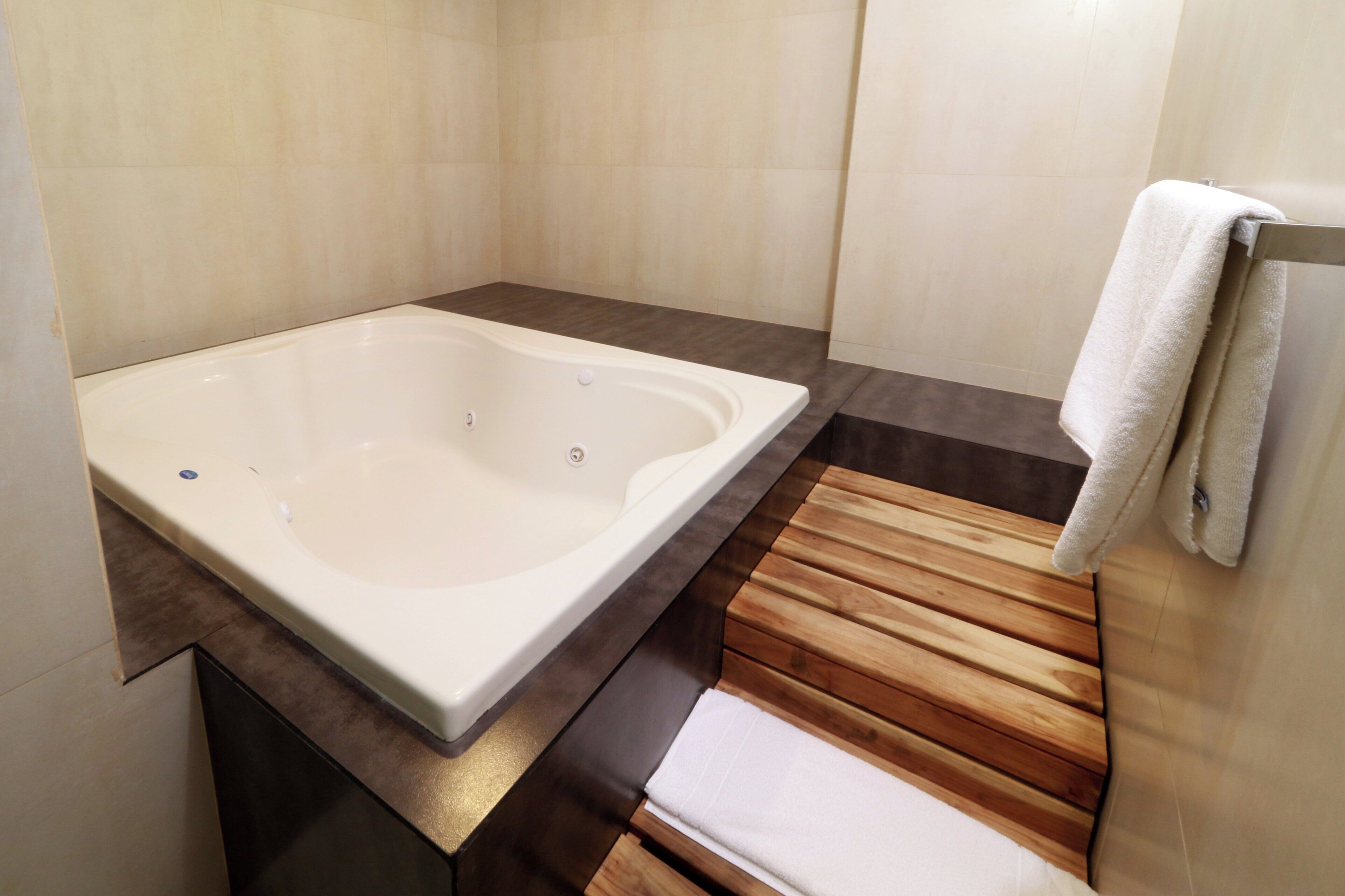 A modern bathroom with a freestanding bathtub, wooden bench, and a towel rack.