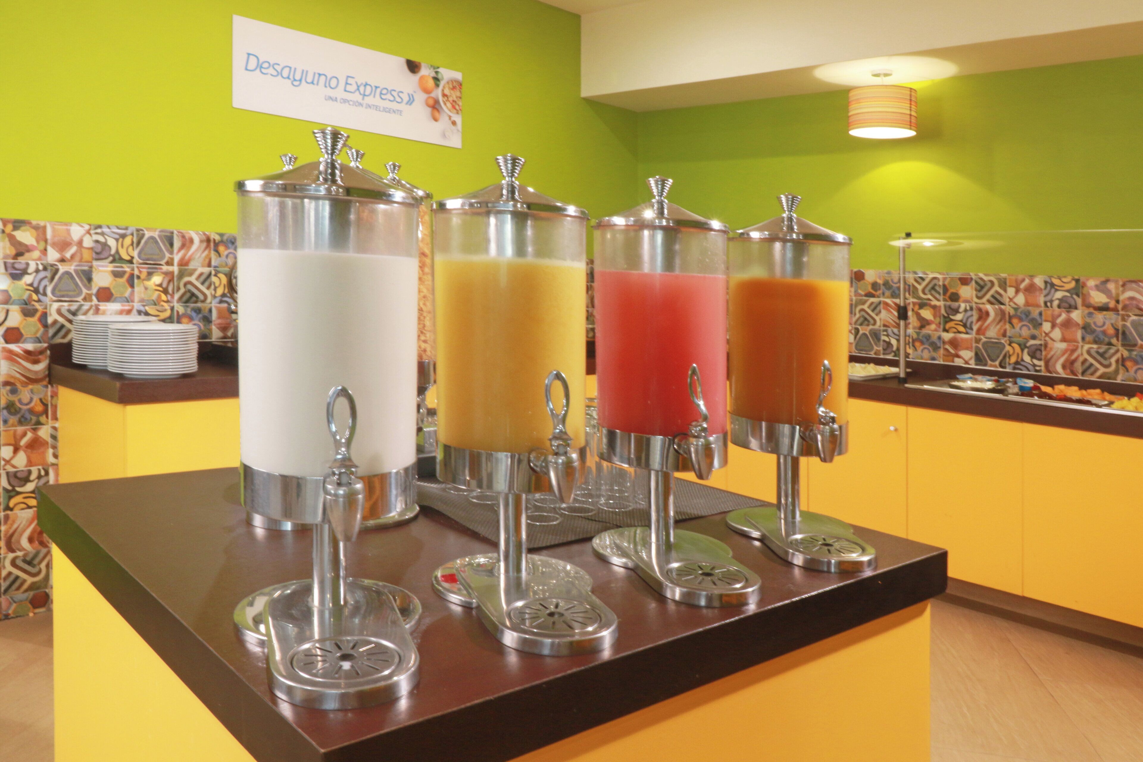 Una estación de bebidas con dispensadores para leche, jugo de naranja y otras dos opciones.