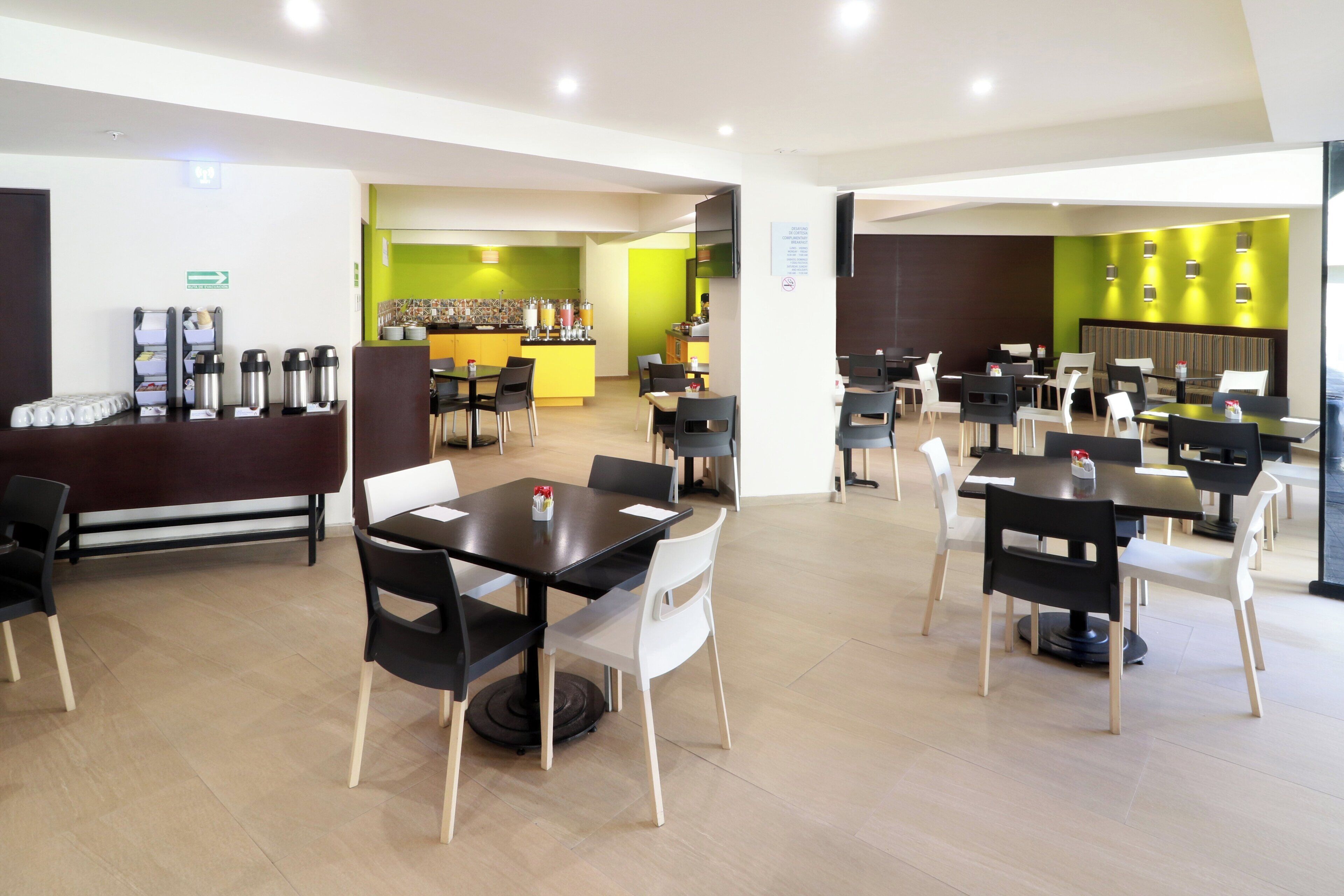 A modern dining area with multiple tables and chairs, a counter with a beverage station, and a green accent wall.