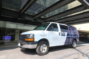 A white van with "SERVICIO GRATUITO FREE SERVICE" and "Holiday Inn Express" branding parked in front of a building with a glass facade. - Holiday Inn Express Mexico Aeropuerto by IHG (Mexico City)
