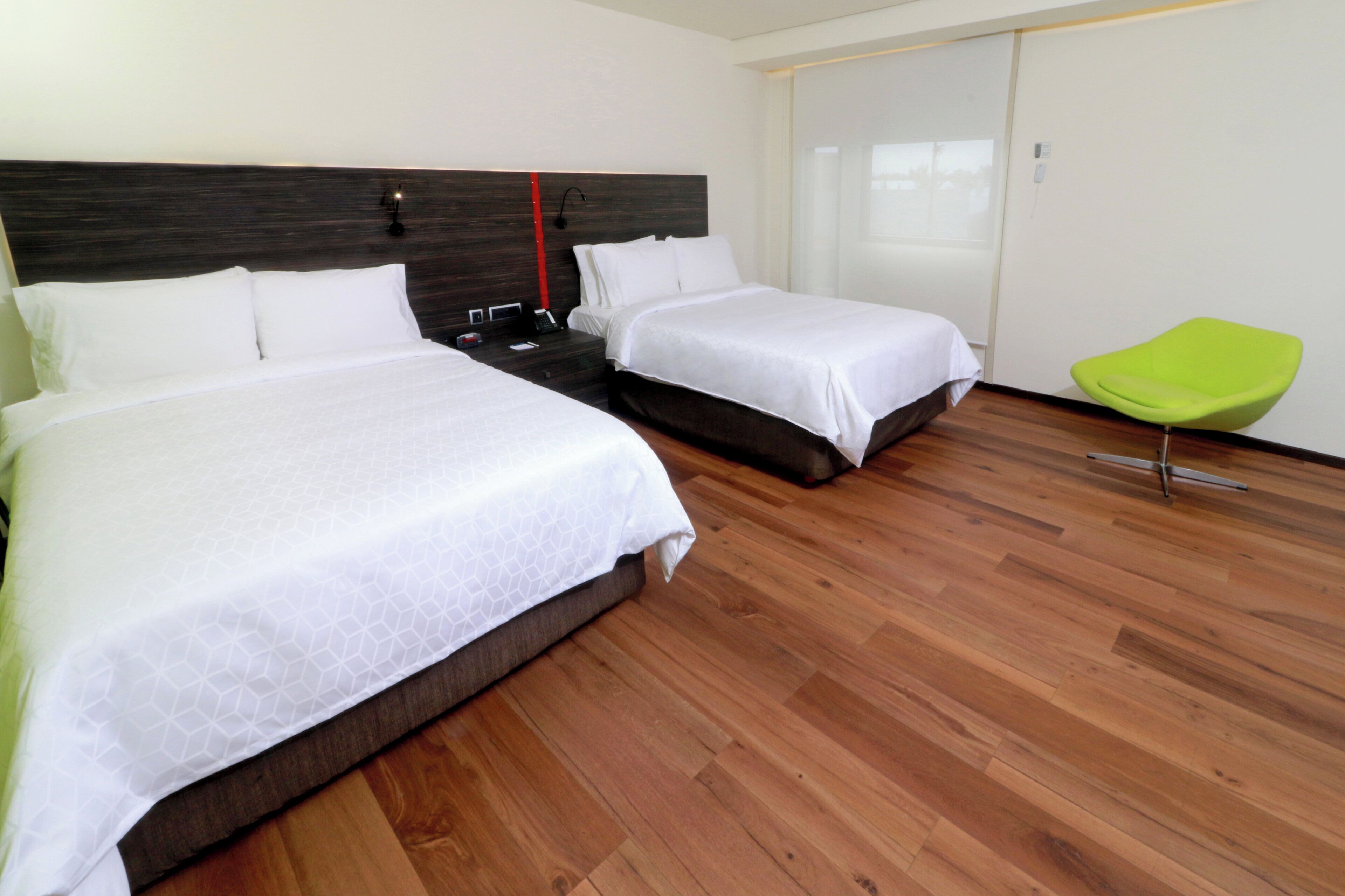 Habitación de hotel con dos camas, suelo de madera, una silla verde y un armario.