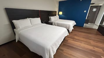 A hotel room with two beds, a dark headboard, a blue accent wall, and a wooden floor.