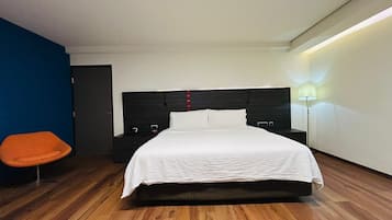 A modern hotel room with a large bed, a nightstand, a chair, and a bedside table.