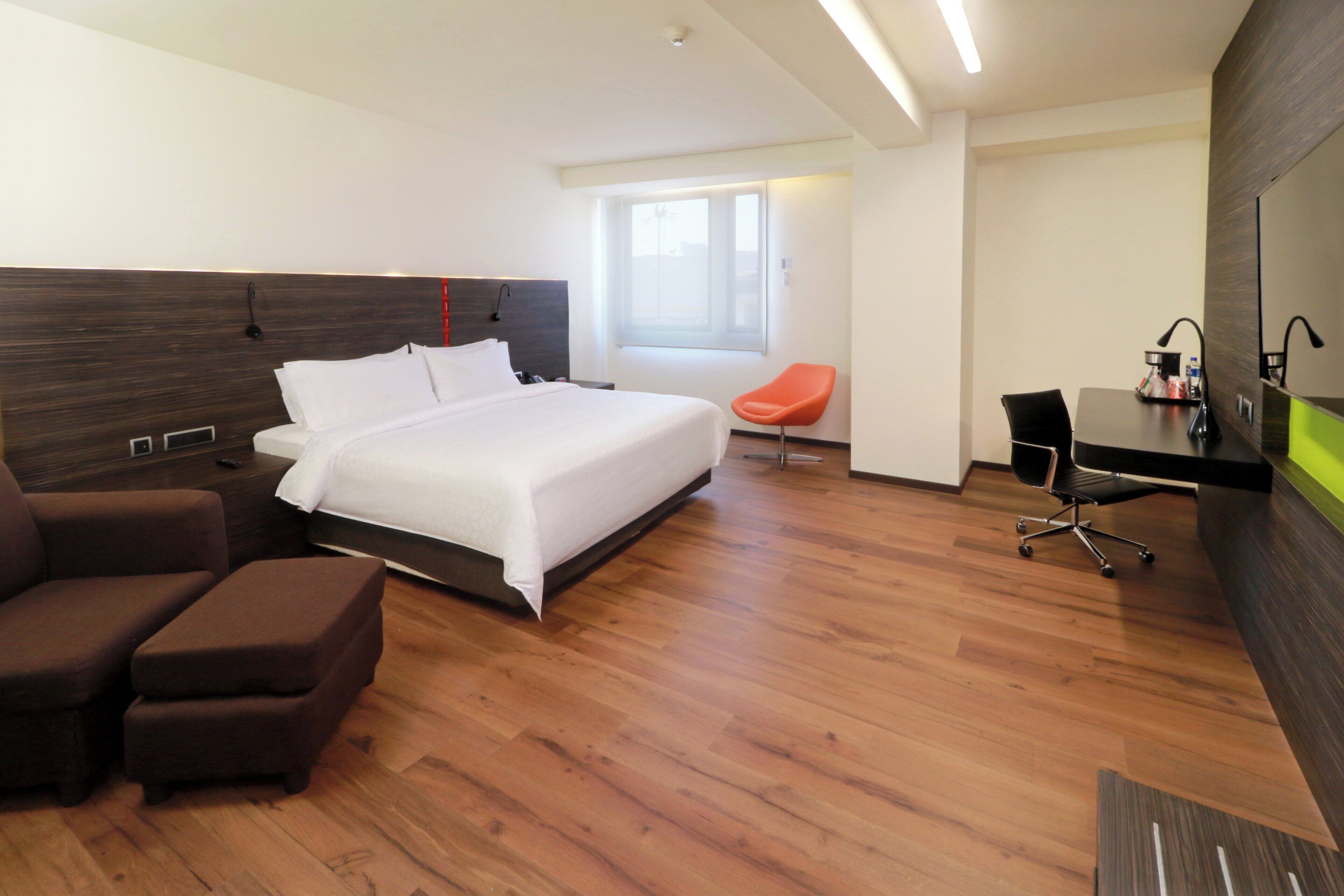 A modern hotel room with a large bed, a desk, a chair, and a television.