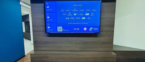 A digital display in a modern hotel lobby with a blue interface listing hotel brands and amenities.