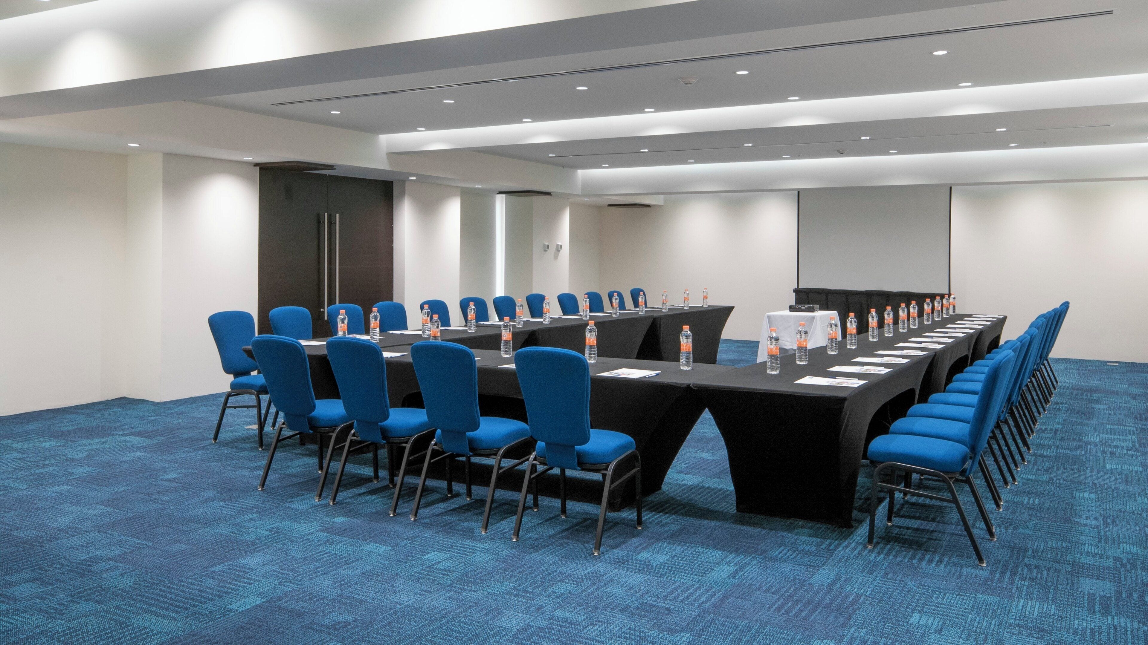 A conference room with a long table, blue chairs, and water bottles.
