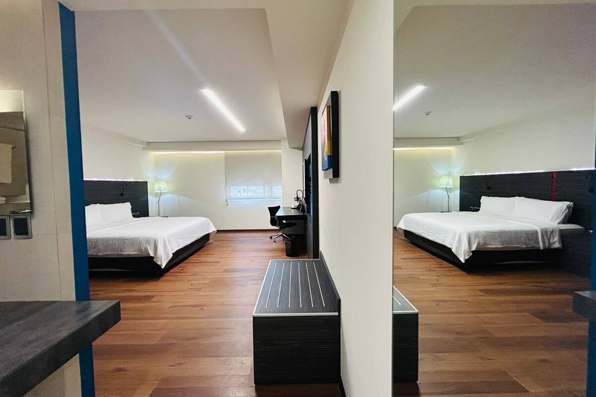A hotel room with two beds, a desk, and a chair.