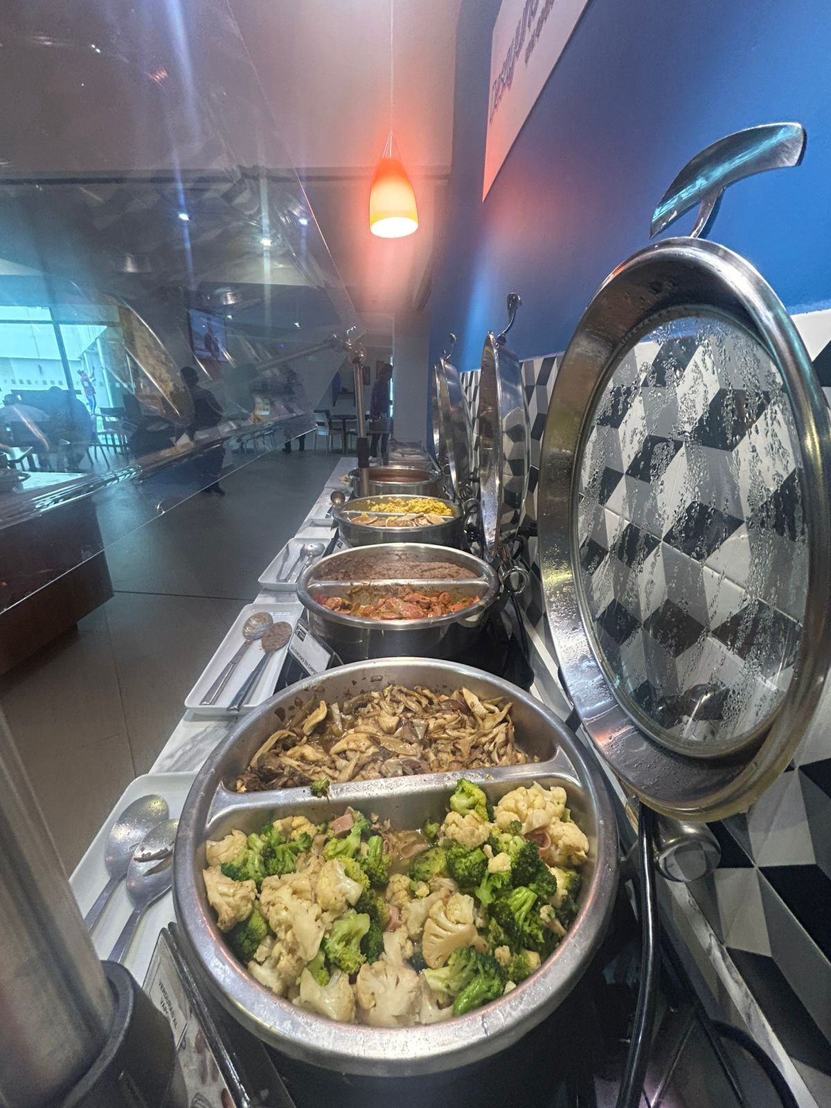 A buffet line with various food options, including vegetables and meats, in a well-lit indoor setting.