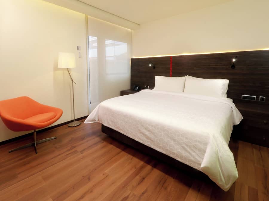 A modern hotel room with a large bed, a bright orange chair, and a wooden floor.