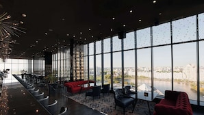 A modern hotel lobby with a long reception desk, seating area, and large windows offering a city view.