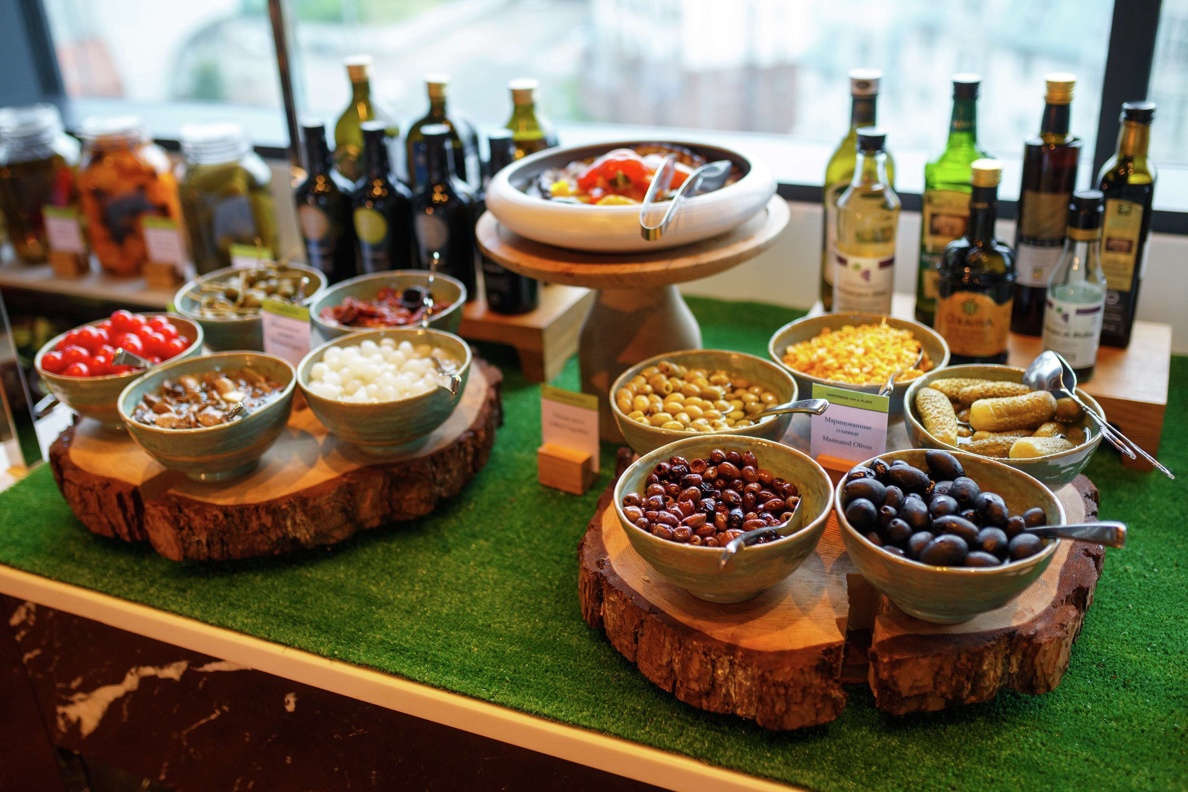 Un bufé con diversos alimentos y botellas de aceite de oliva sobre pedestales de madera.