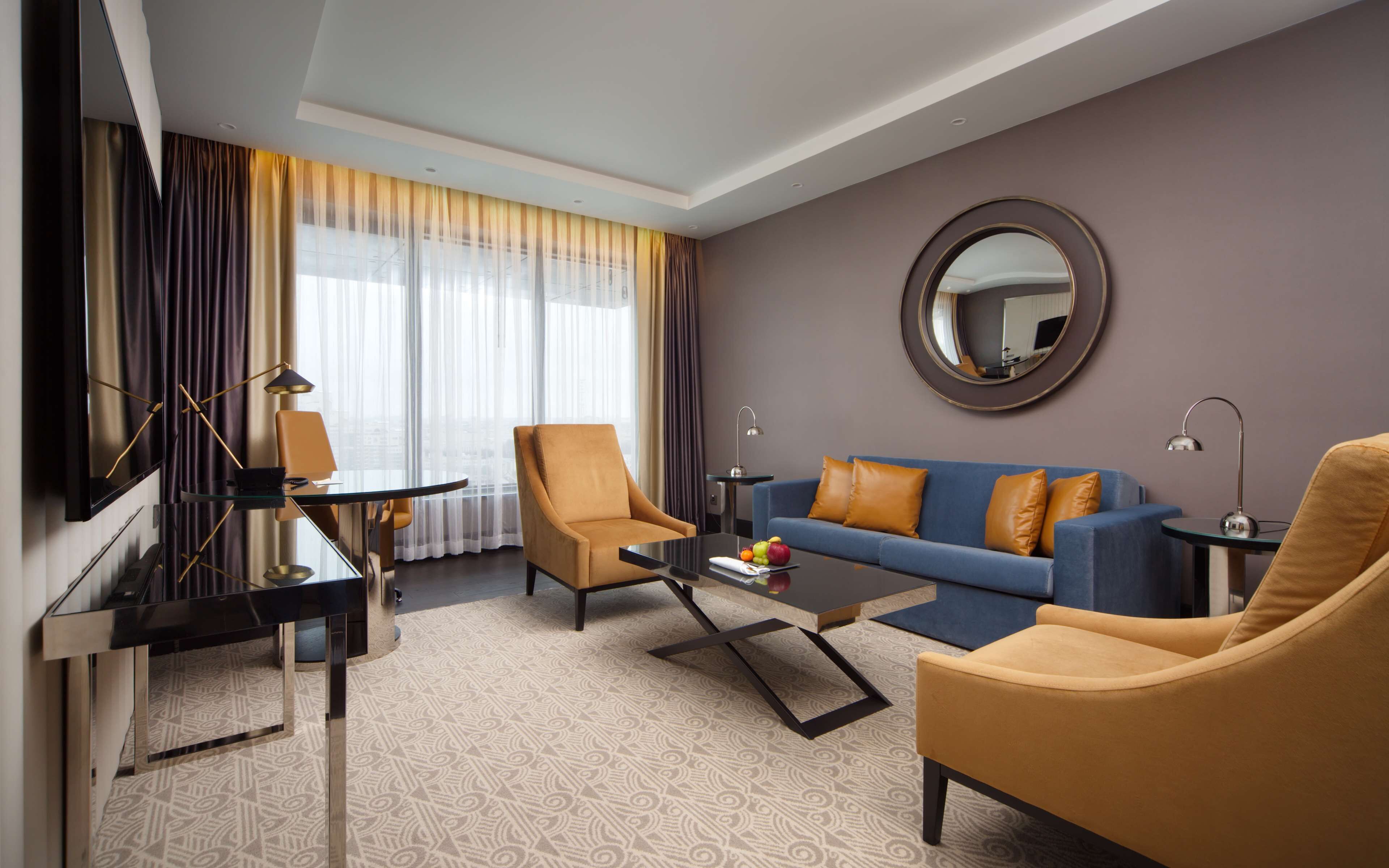 Een moderne hotelkamer met een zithoek, compleet met een bank, fauteuils, een salontafel, een televisie en een piano.
