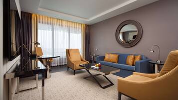 Een moderne hotelkamer met een zithoek, compleet met een bank, fauteuils, een salontafel, een televisie en een piano.