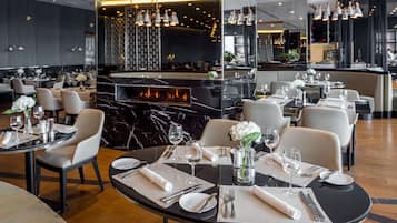 Een modern restaurant met ronde tafels, witte stoelen en een centraal geplaatst haardvuur.