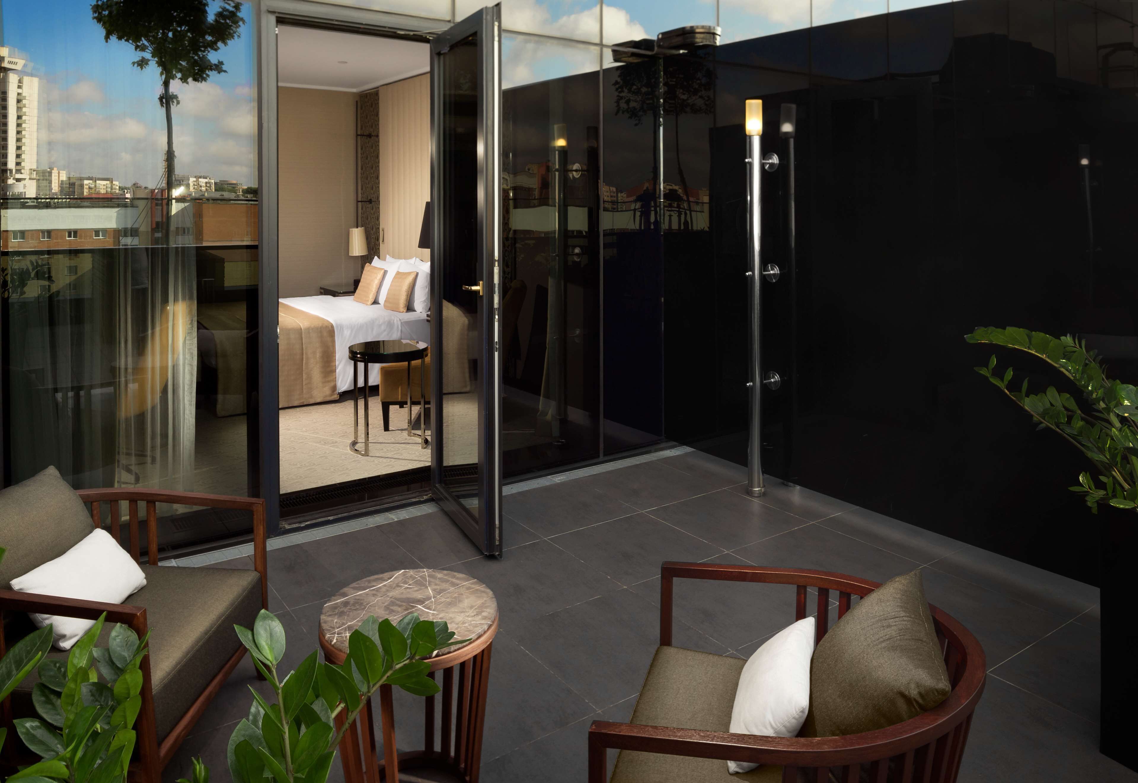 Ein modernes Hotelzimmer mit Balkon, ausgestattet mit einer Couch, Sesseln und einem kleinen Tisch.
