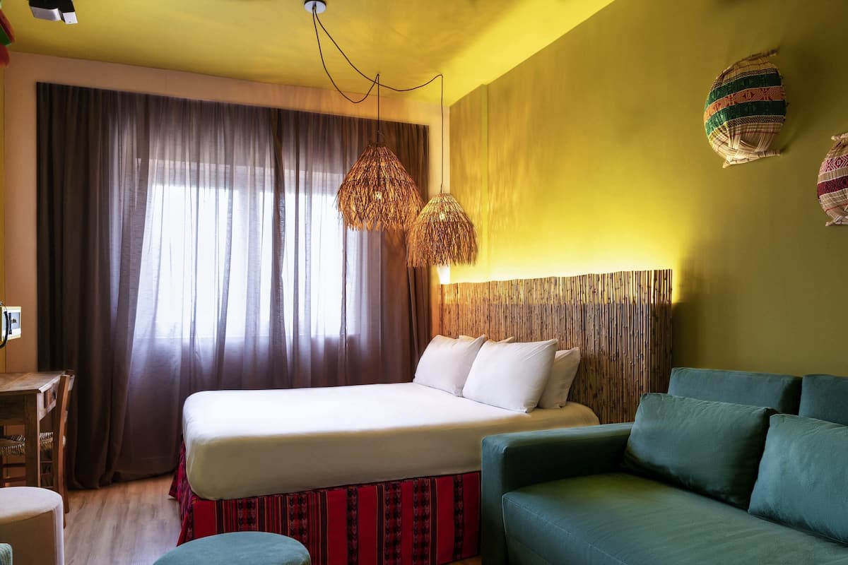 Een slaapkamer met een bed, een bank, een bureau en een groot raam met gordijnen.