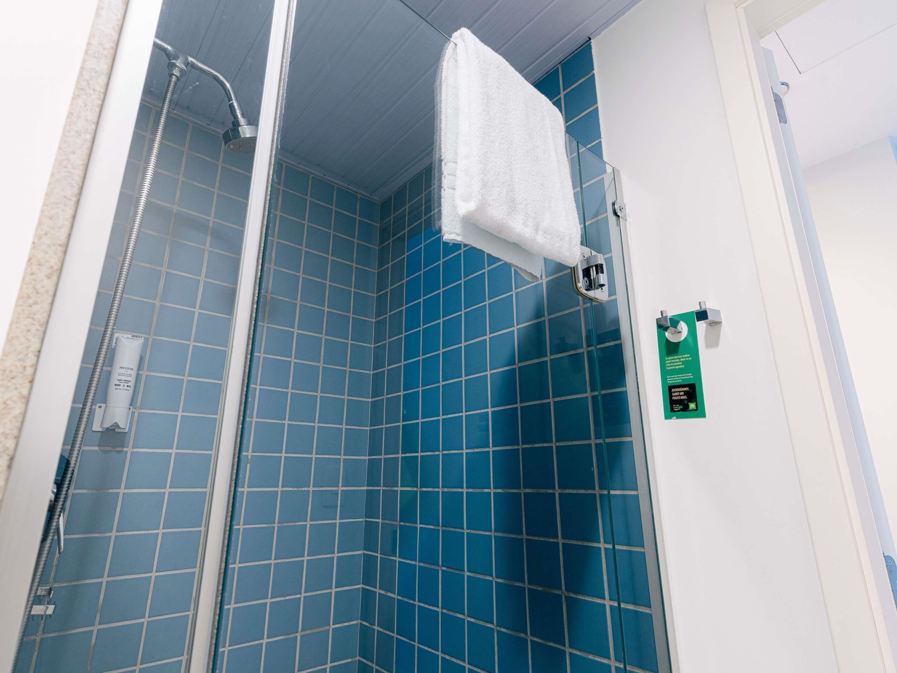 A bathroom with blue tiles, a shower, and a white towel hanging on a rack.