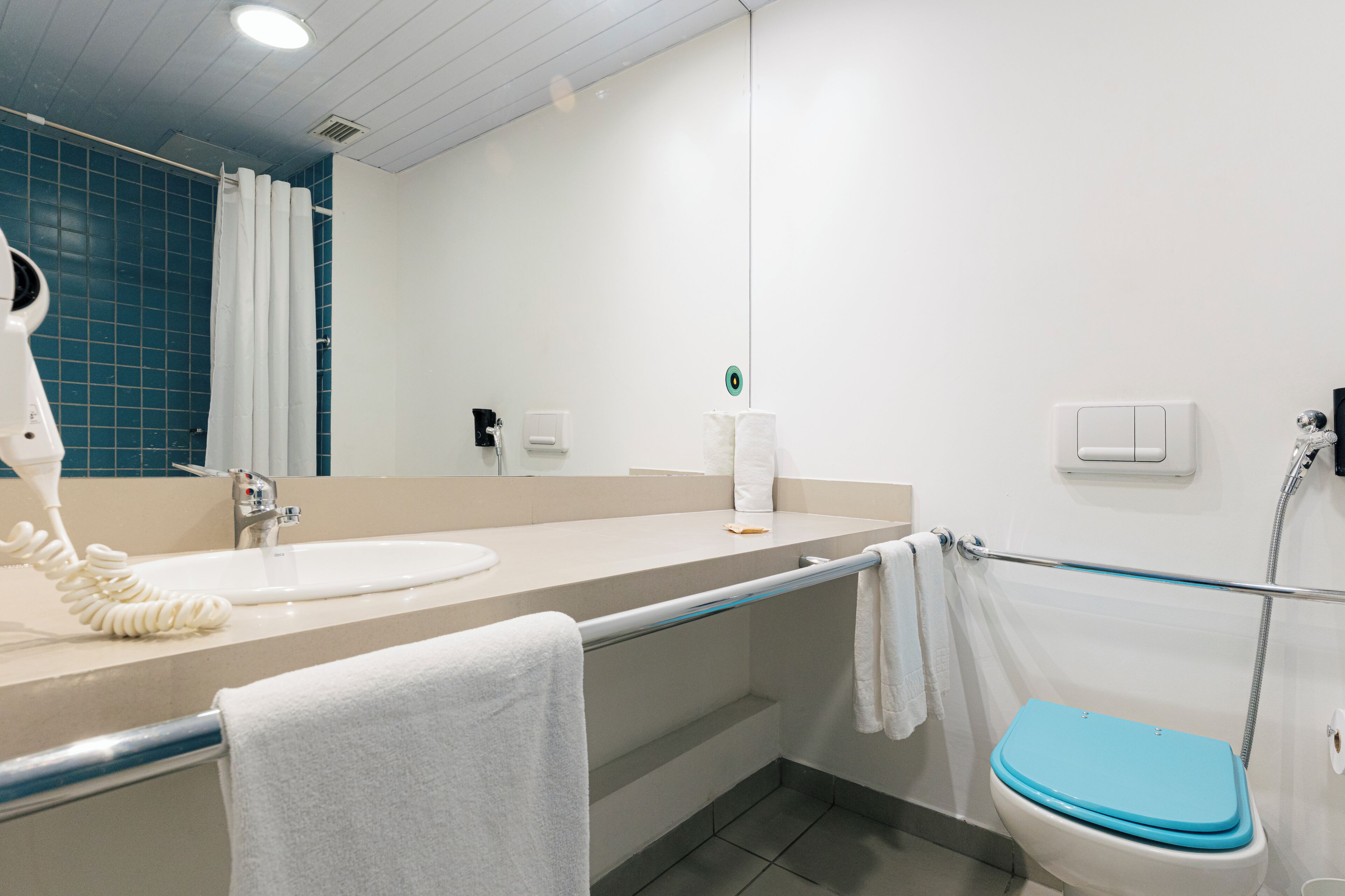 A bathroom with a white sink, a towel rack, a toilet, and a shower area.