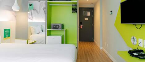 Ein Hotelzimmer mit Bett, Schreibtisch mit Telefon, Fernseher, Klimaanlage und grüner Wand.