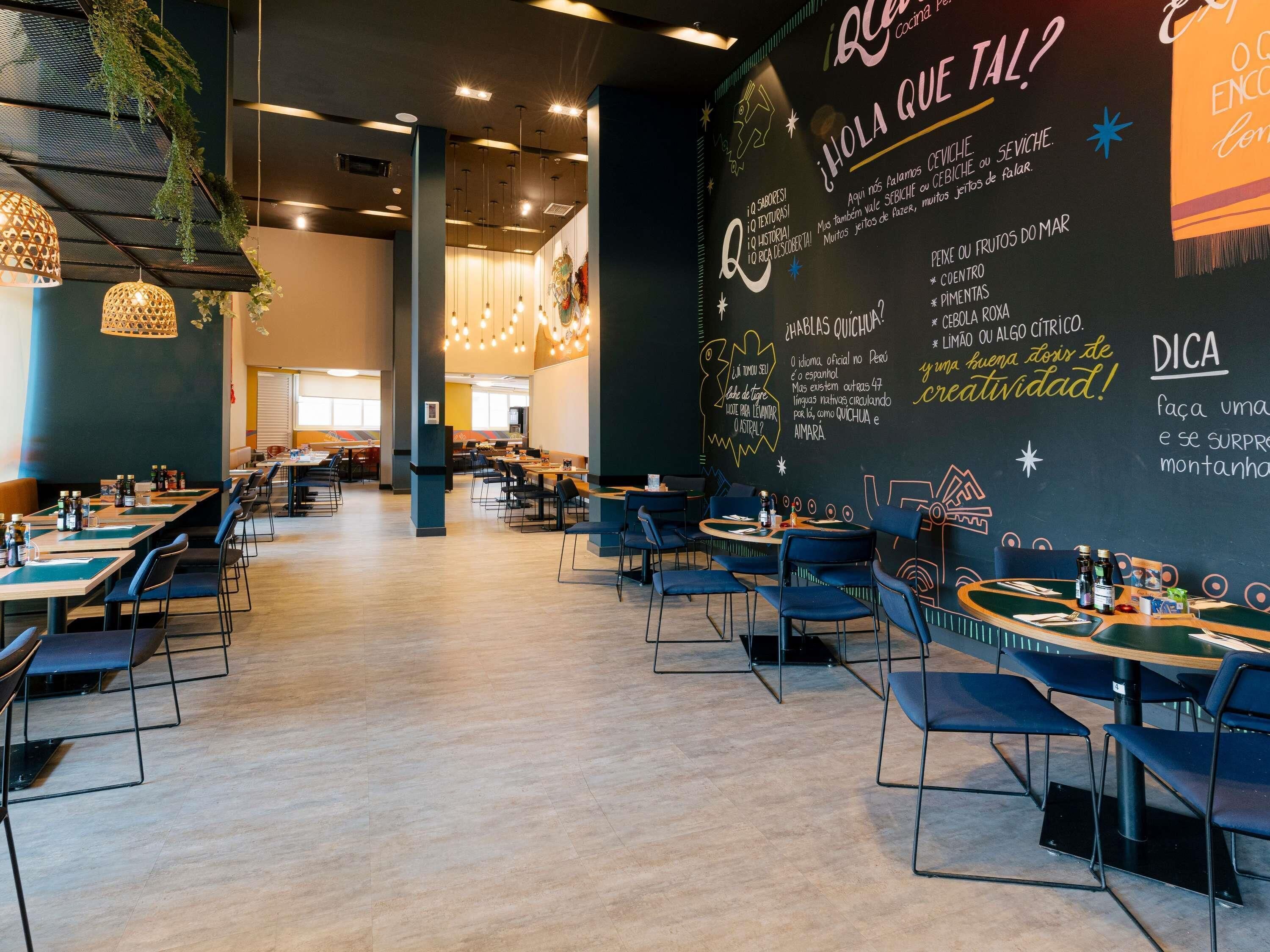 A restaurant with tables and chairs, a chalkboard menu, and hanging lights.