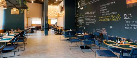 A restaurant with tables and chairs, a chalkboard menu, and hanging lights.