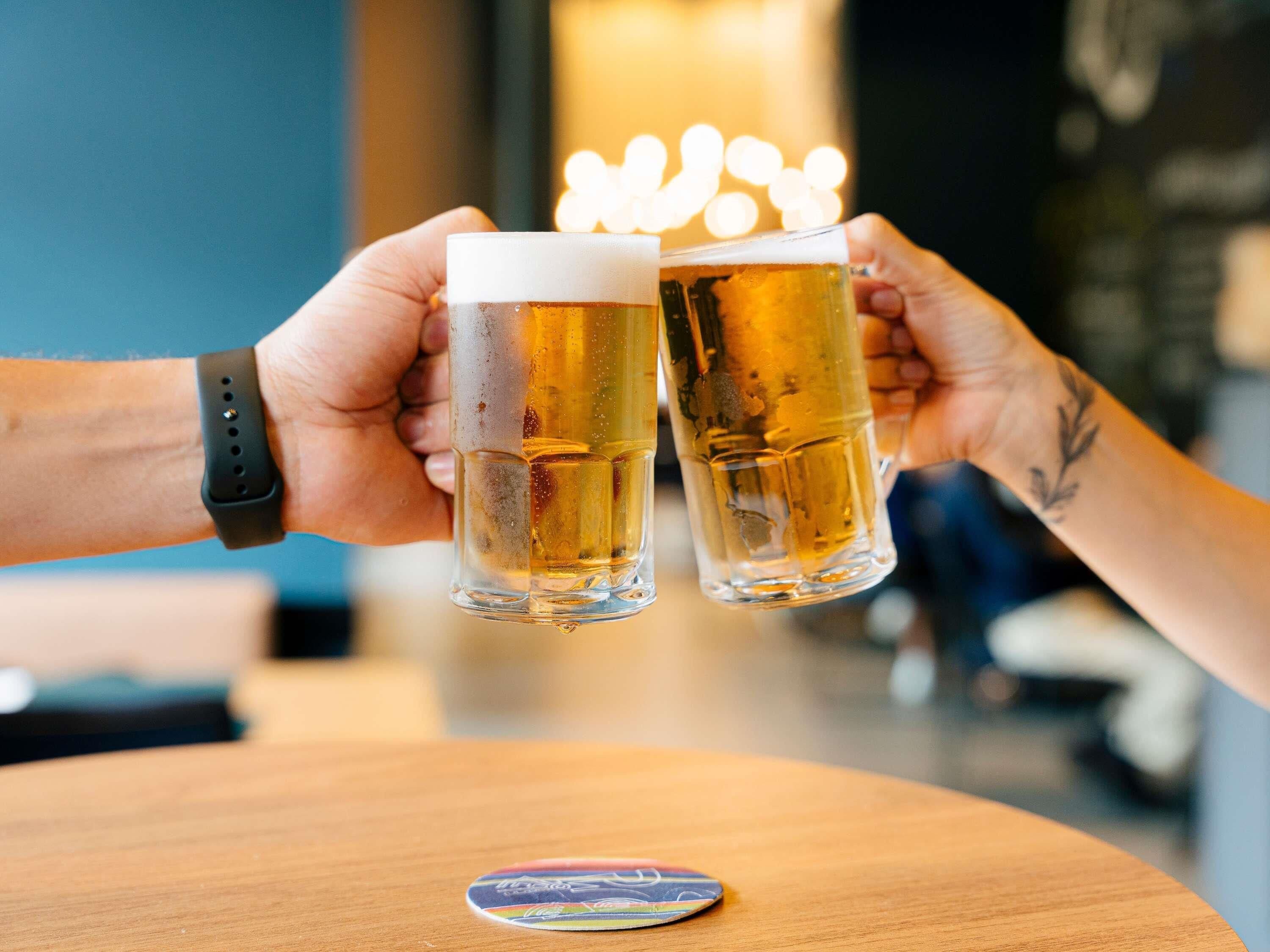 Due persone che brindano con delle birre al bancone di un bar.