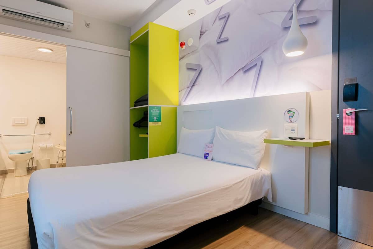 Een hotelkamer met een bed, een groen opbergmeubel, een wit hoofdeinde en een wandlamp.
