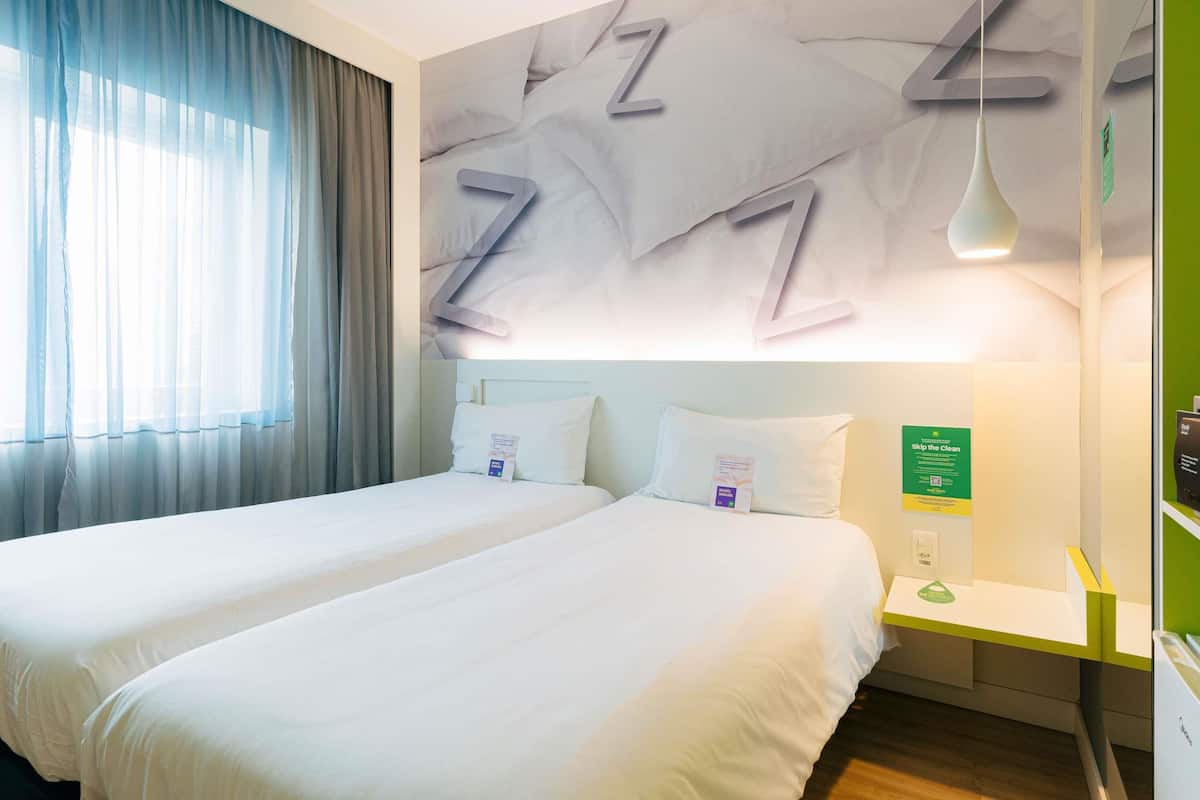 Een hotelkamer met twee bedden, een groene accentmuur, een nachtkastje en een wandlamp.
