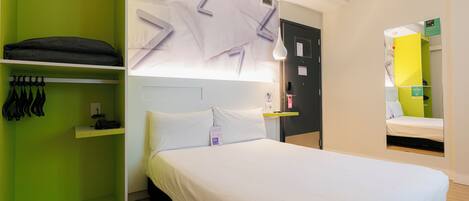 Une chambre d’hôtel moderne avec un lit, une armoire verte et un miroir qui reflète une autre pièce.
