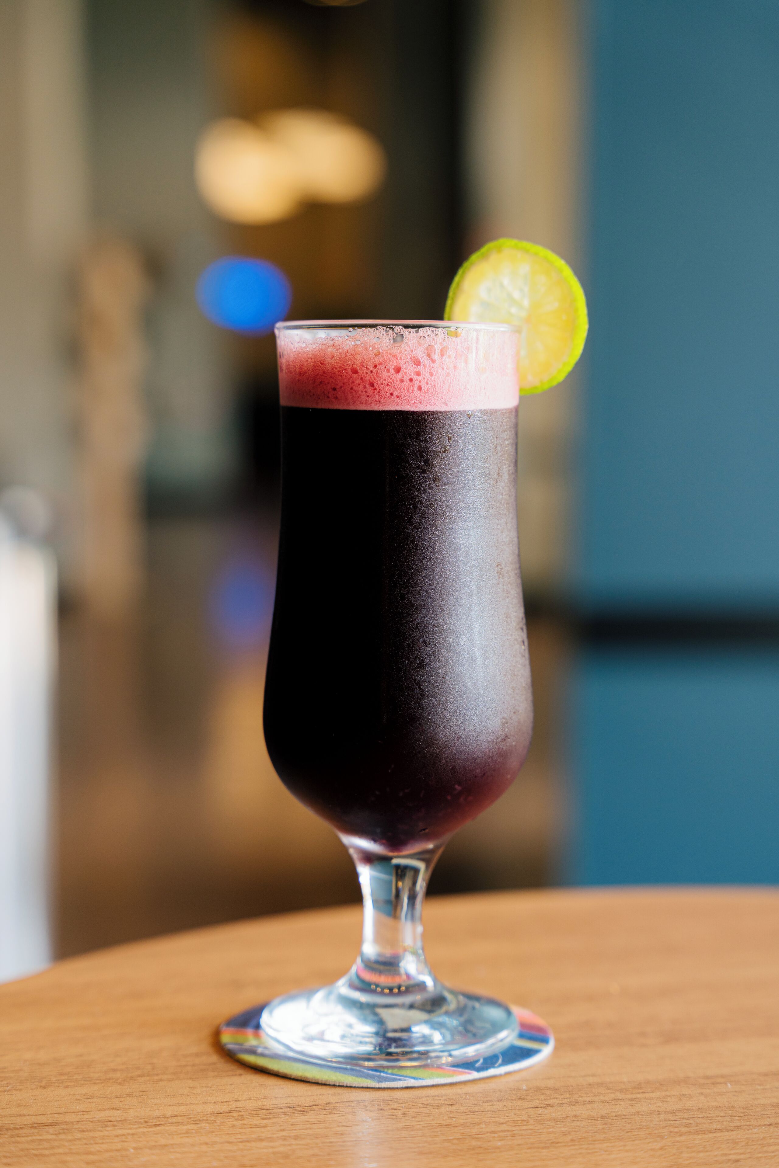 A glass of dark-colored beverage with a lime garnish on a wooden table.