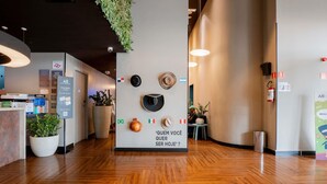 Un hall d’hôtel avec un plancher en bois, un comptoir d’accueil, une plante fixée au mur et un panneau affichant une question en portugais.