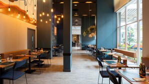 Un intérieur de restaurant moderne, caractérisé par de hauts plafonds, des luminaires suspendus et de grandes fenêtres.