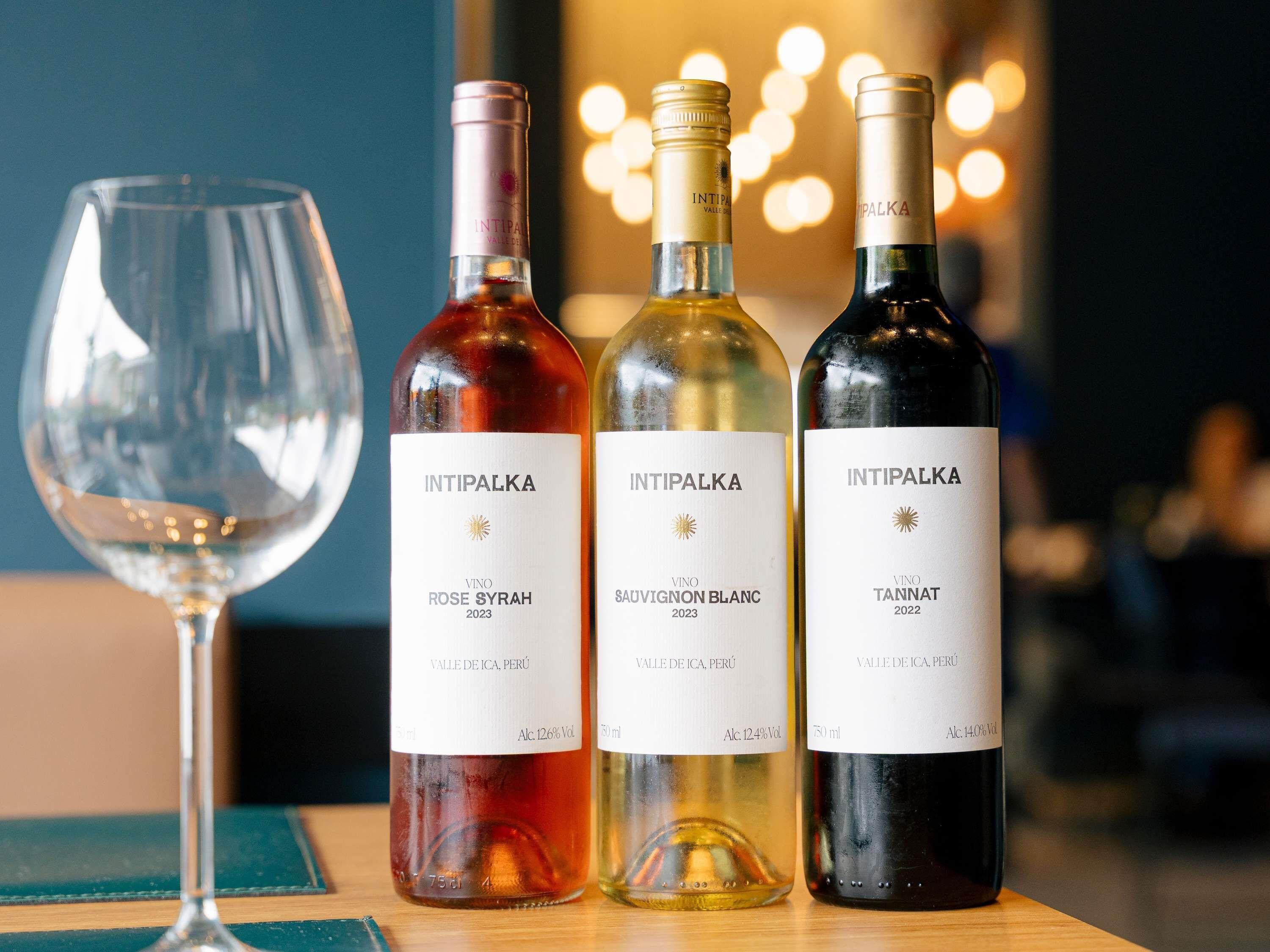 Three bottles of wine and a wine glass on a table.