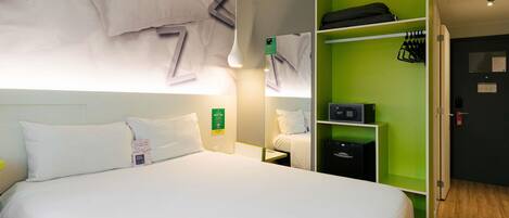 A hotel room with a bed, a green wardrobe, a desk, and a wall-mounted air conditioning unit.
