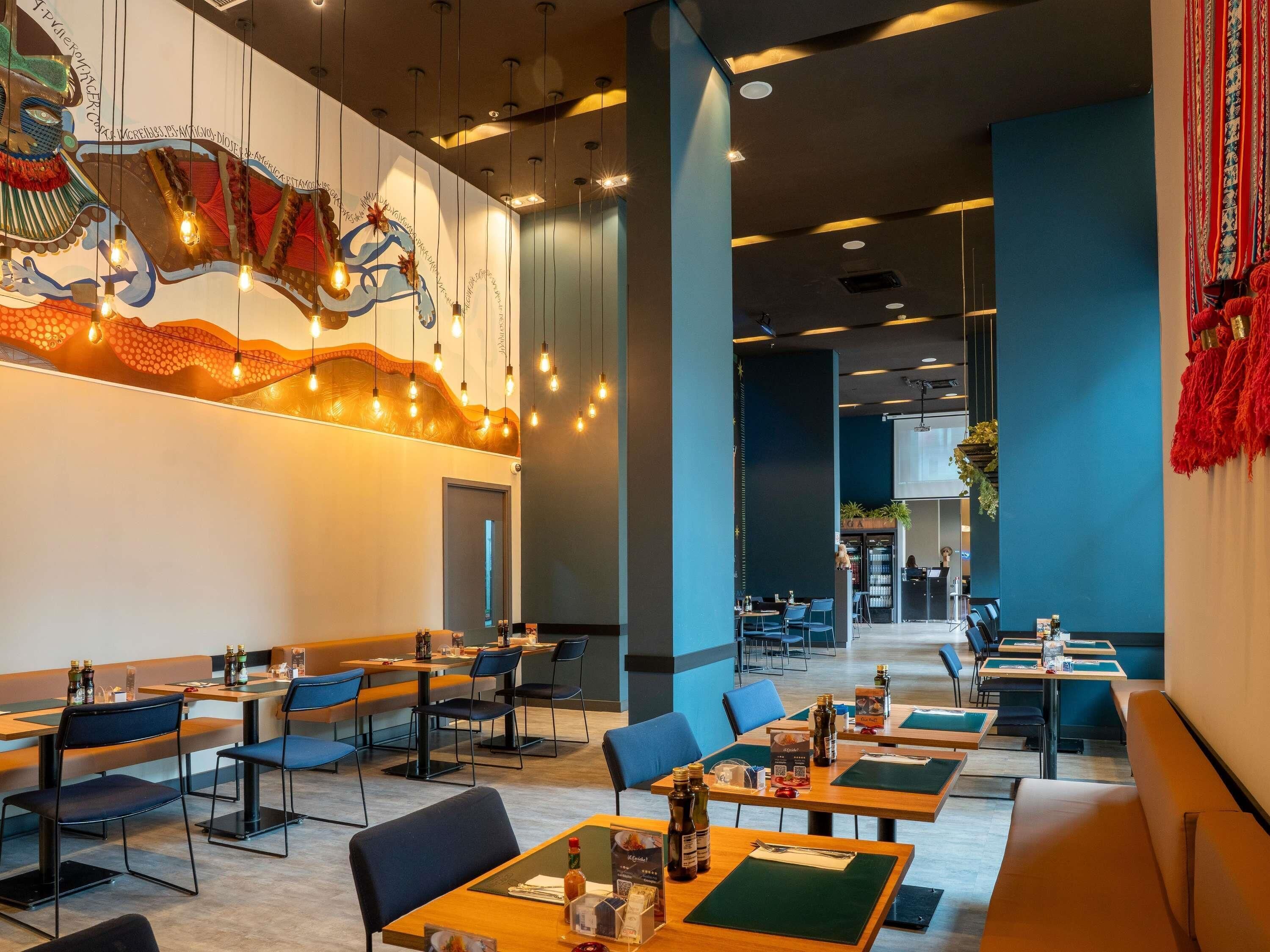 A modern restaurant with booths and tables, hanging lights, and a decorative wall mural.