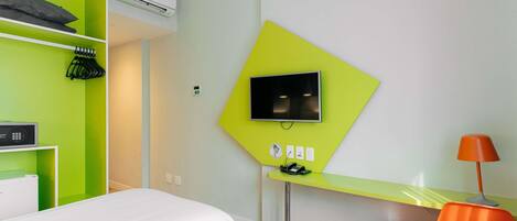 A hotel room with a bed, a desk with a computer, a TV, and a chair.