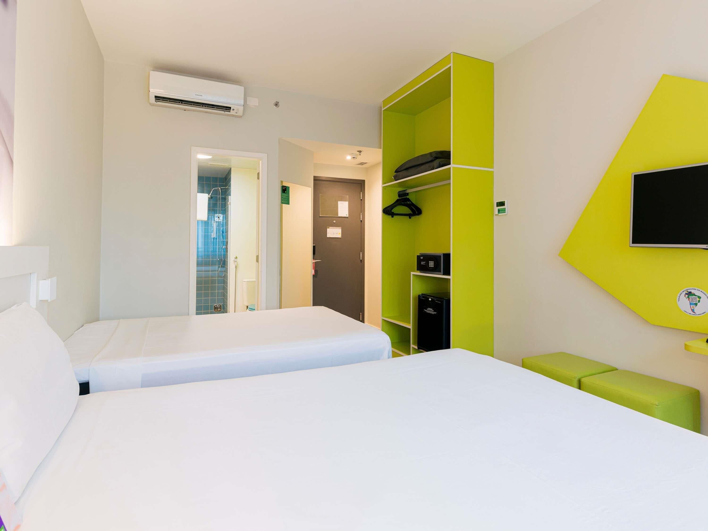 Une chambre d’hôtel équipée d’un lit, d’un meuble de rangement vert, d’une télévision et d’un climatiseur.