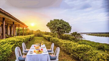 Un área de comedor al aire libre con una mesa lista para dos personas, rodeada de abundante vegetación y vistas a un río.